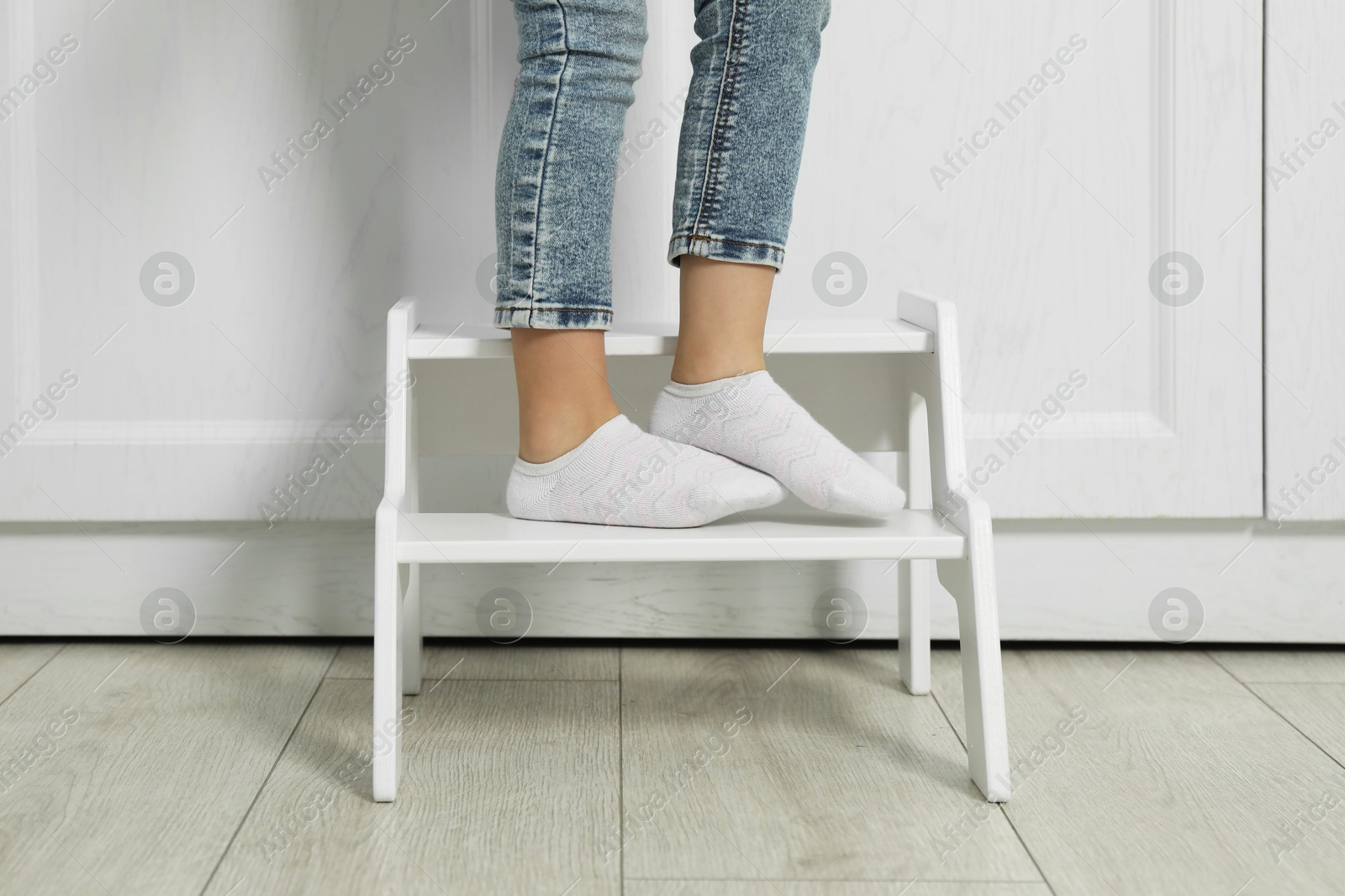 Photo of Little girl standing on step stool indoors, closeup