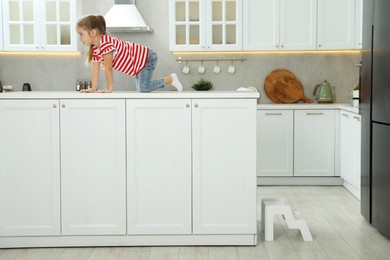 Photo of Little girl sitting on counter near step stool in kitchen