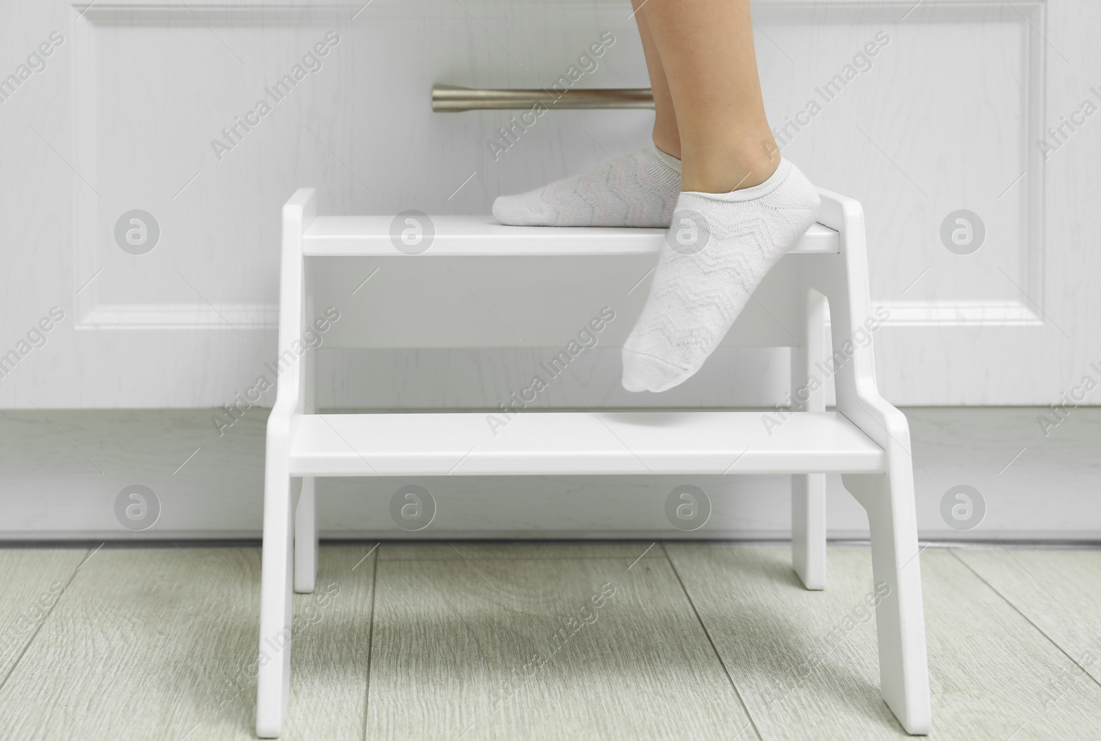 Photo of Little girl standing on step stool indoors, closeup