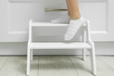 Photo of Little girl standing on step stool indoors, closeup