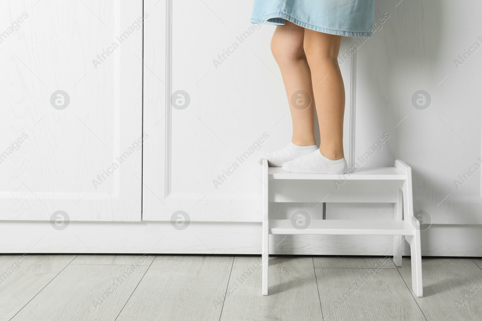 Photo of Little girl standing on step stool indoors, closeup. Space for text