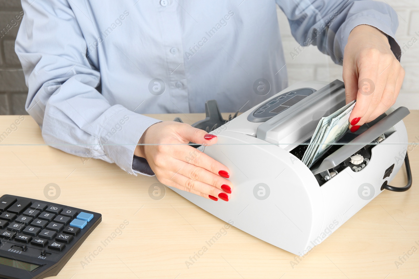 Photo of Cashier using money counting machine at table in currency exchange, closeup