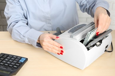 Photo of Cashier using money counting machine at table in currency exchange, closeup