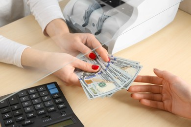 Photo of Cashier giving dollar banknotes to client at table in money exchange, closeup