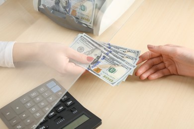 Photo of Cashier giving dollar banknotes to client at table in money exchange, closeup