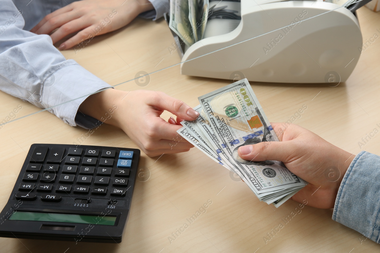 Photo of Client giving dollar banknotes to cashier at table in money exchange, closeup