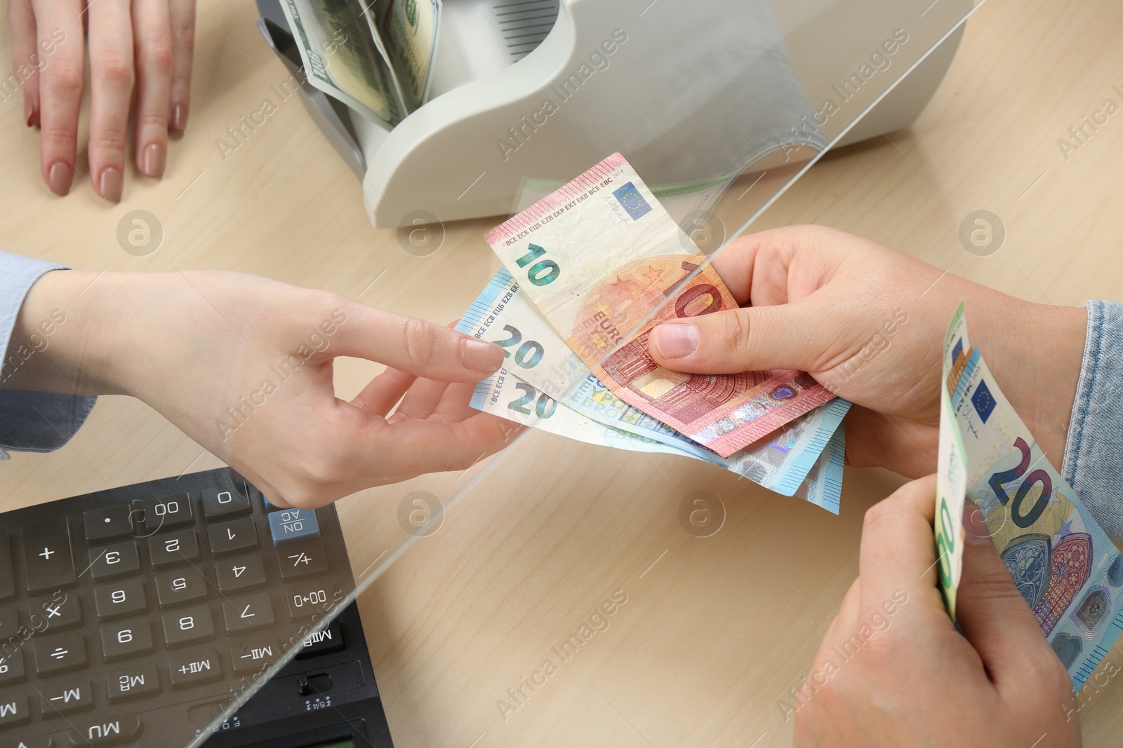 Photo of Client giving euro banknotes to cashier at table in money exchange, closeup