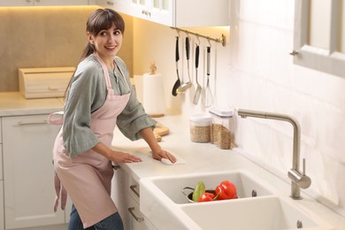 Photo of Woman cleaning countertop with paper towel in kitchen