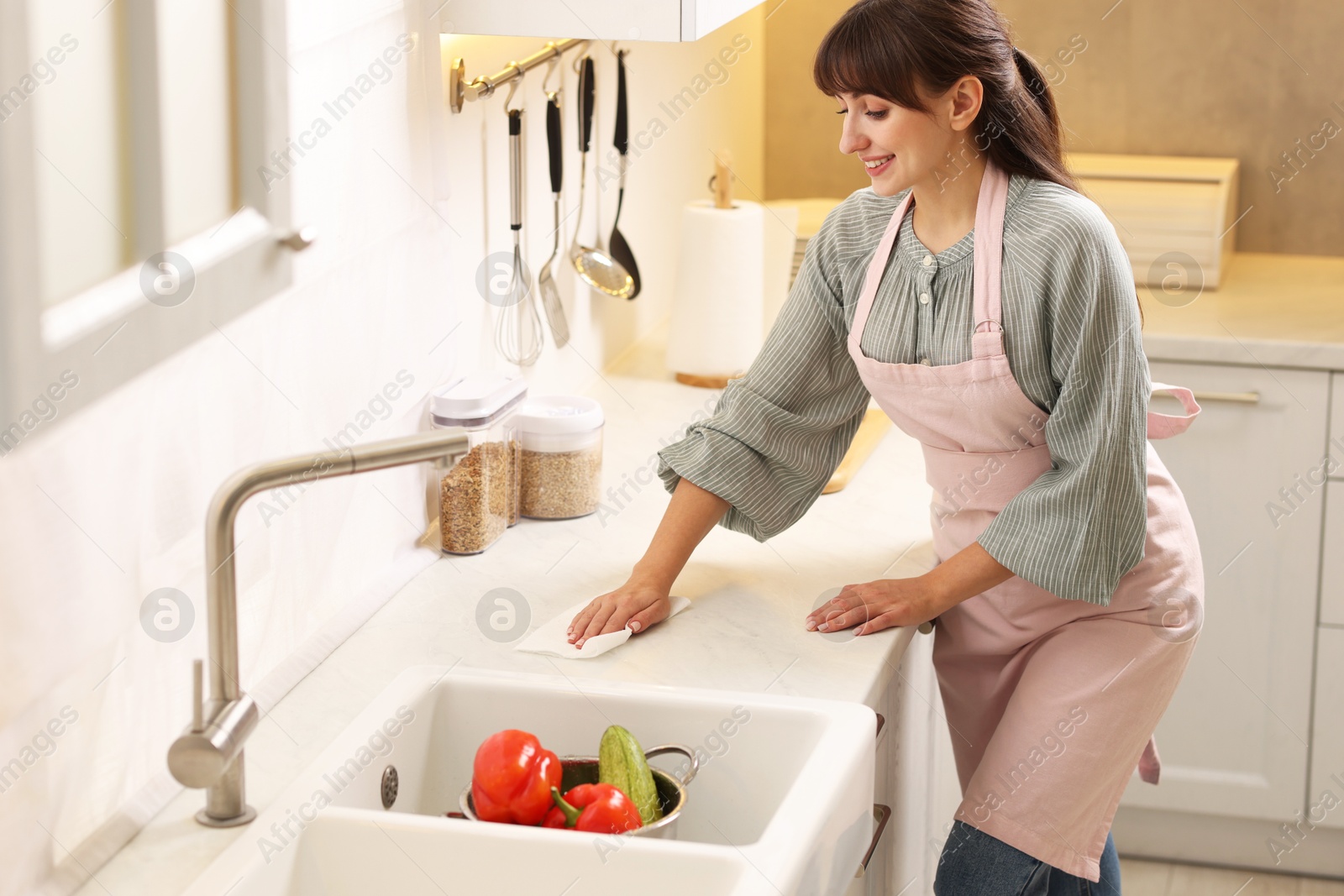 Photo of Smiling woman cleaning countertop with paper towel in kitchen