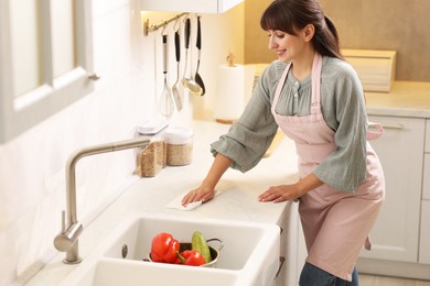 Smiling woman cleaning countertop with paper towel in kitchen