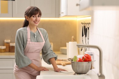 Photo of Smiling woman cleaning countertop with paper towel in kitchen