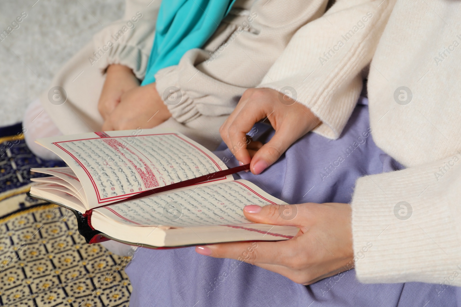 Photo of Muslim woman and her daughter with Quran praying on mat at home, closeup