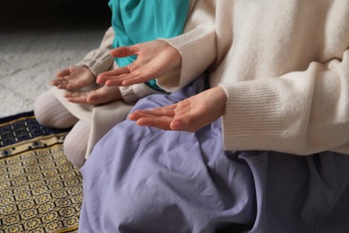 Photo of Muslim woman and her daughter praying on mat at home, closeup