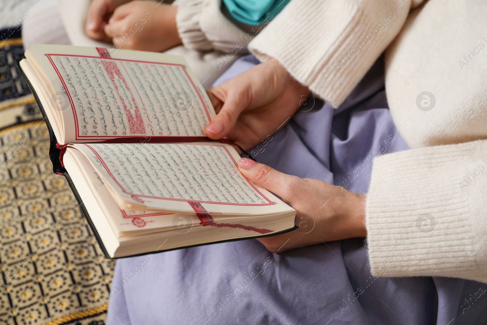 Photo of Muslim woman and her daughter with Quran praying on mat at home, closeup