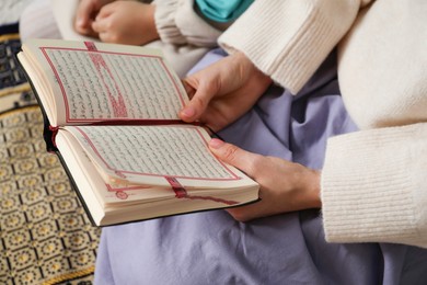 Photo of Muslim woman and her daughter with Quran praying on mat at home, closeup