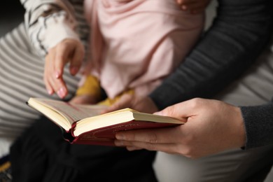 Photo of Muslim family with Quran praying on mat at home, closeup