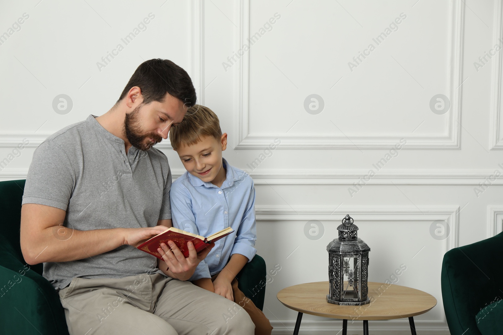 Photo of Muslim man and his son reading Quran at home