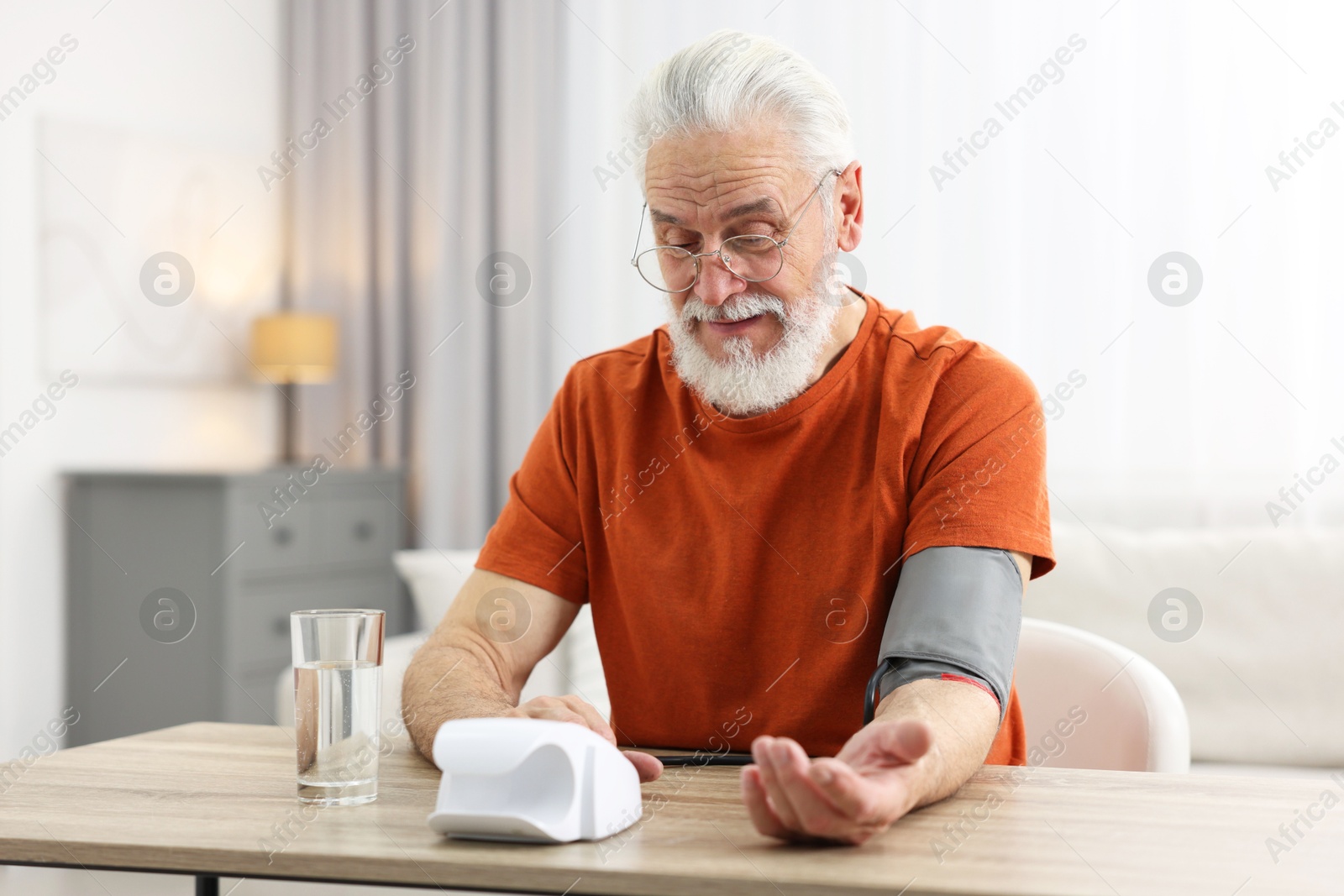 Photo of Senior man measuring blood pressure at table indoors