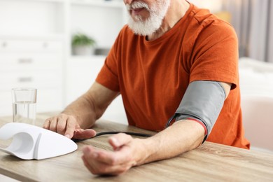 Photo of Senior man measuring blood pressure at table indoors, closeup