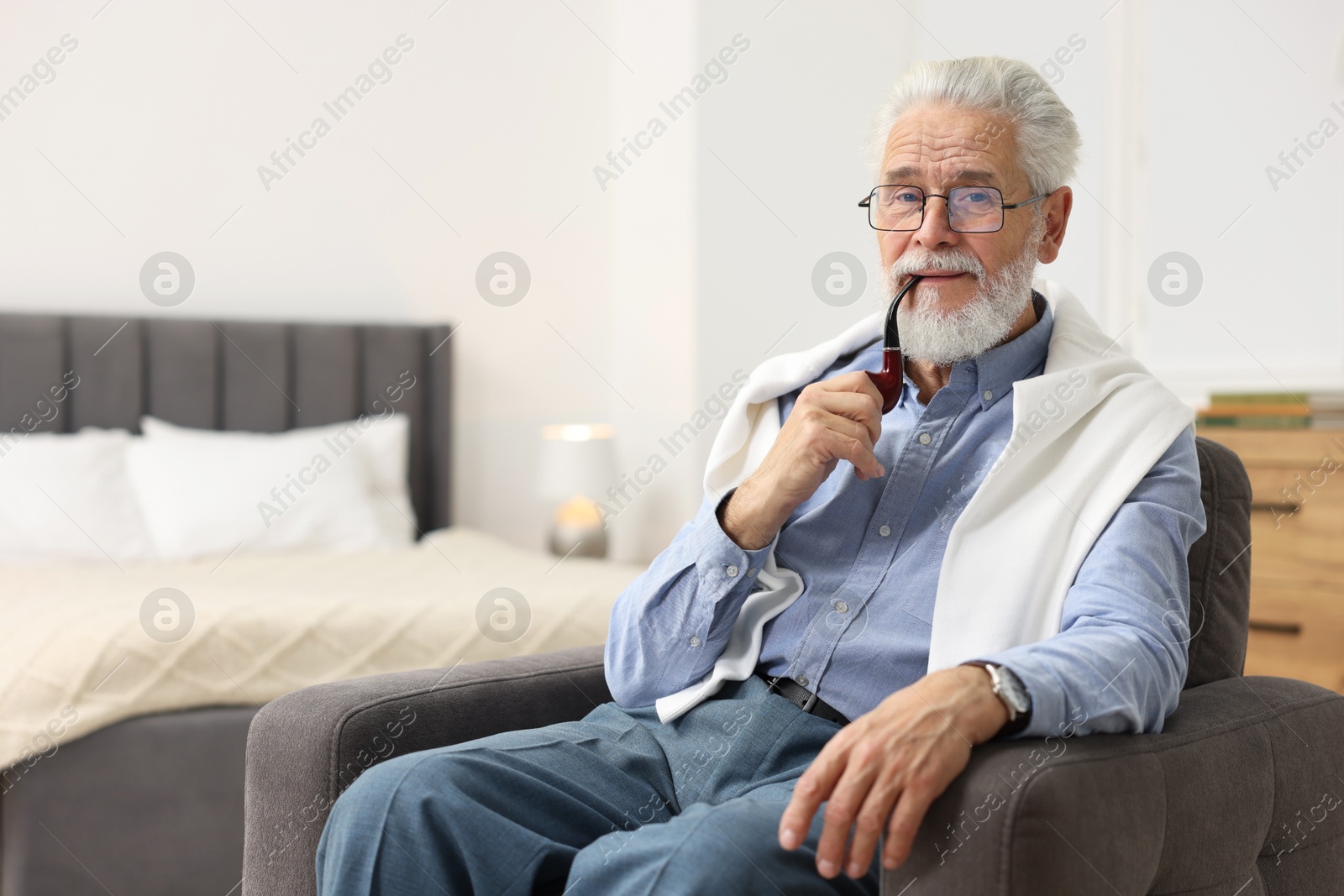 Photo of Handsome bearded man with tobacco pipe in armchair indoors