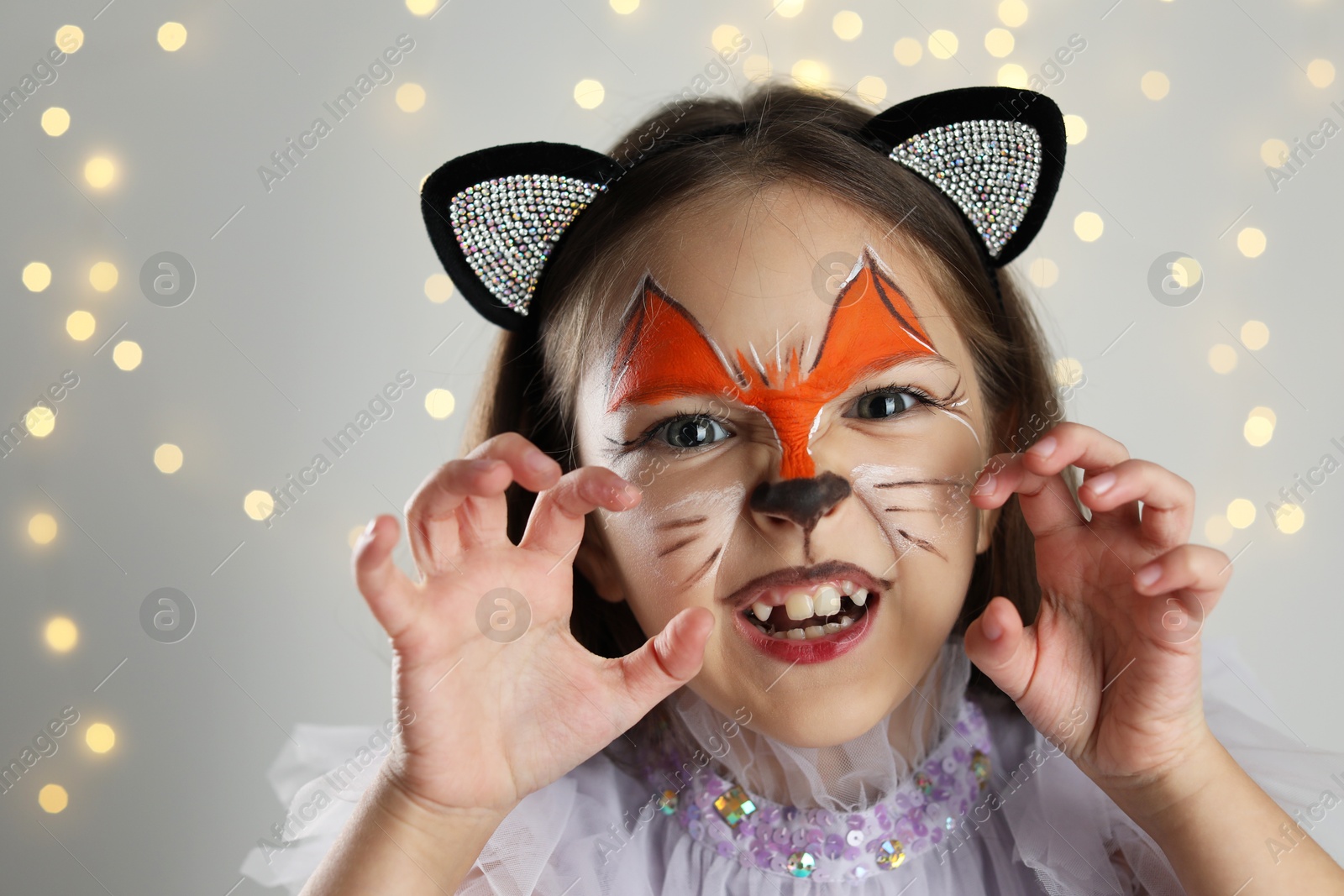 Photo of Cute girl with painted face and ears as cat on grey background with blurred lights