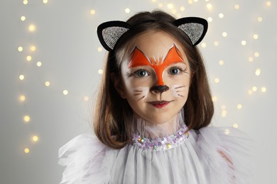 Cute girl with painted face and ears as cat on grey background with blurred lights