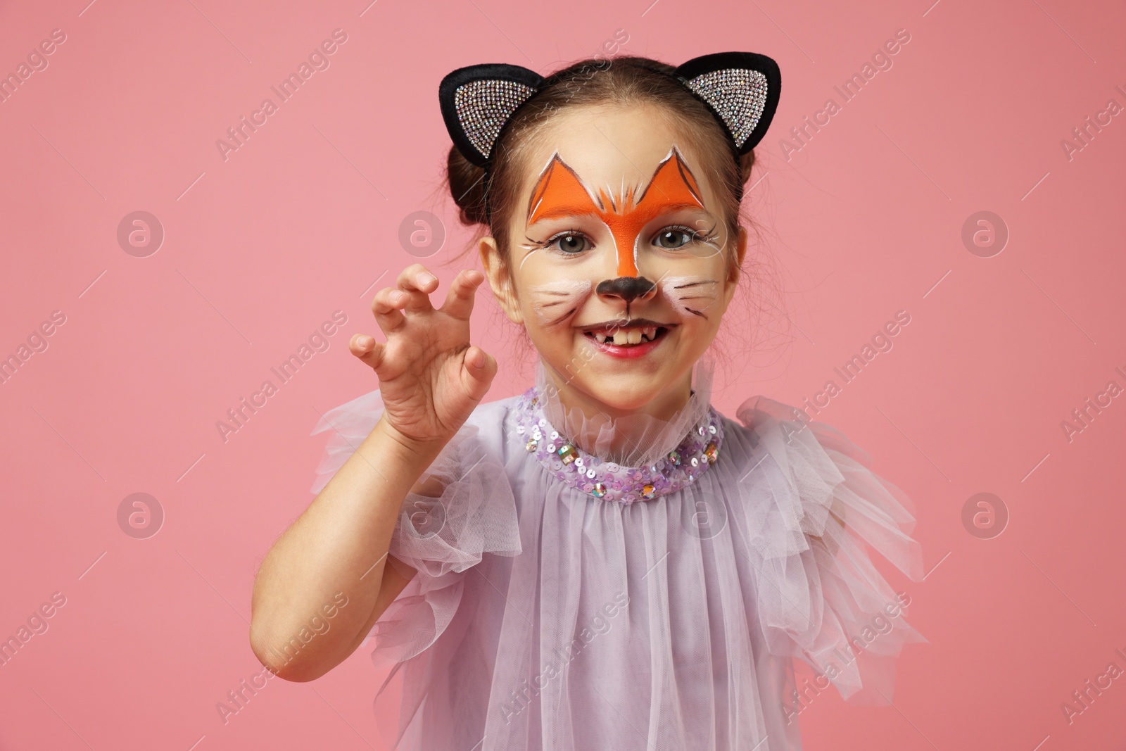 Photo of Cute girl with painted face and ears as cat on pink background