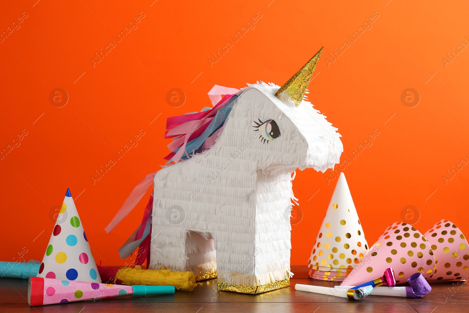 Photo of Bright pinata in shape of unicorn and party accessories on table against orange background