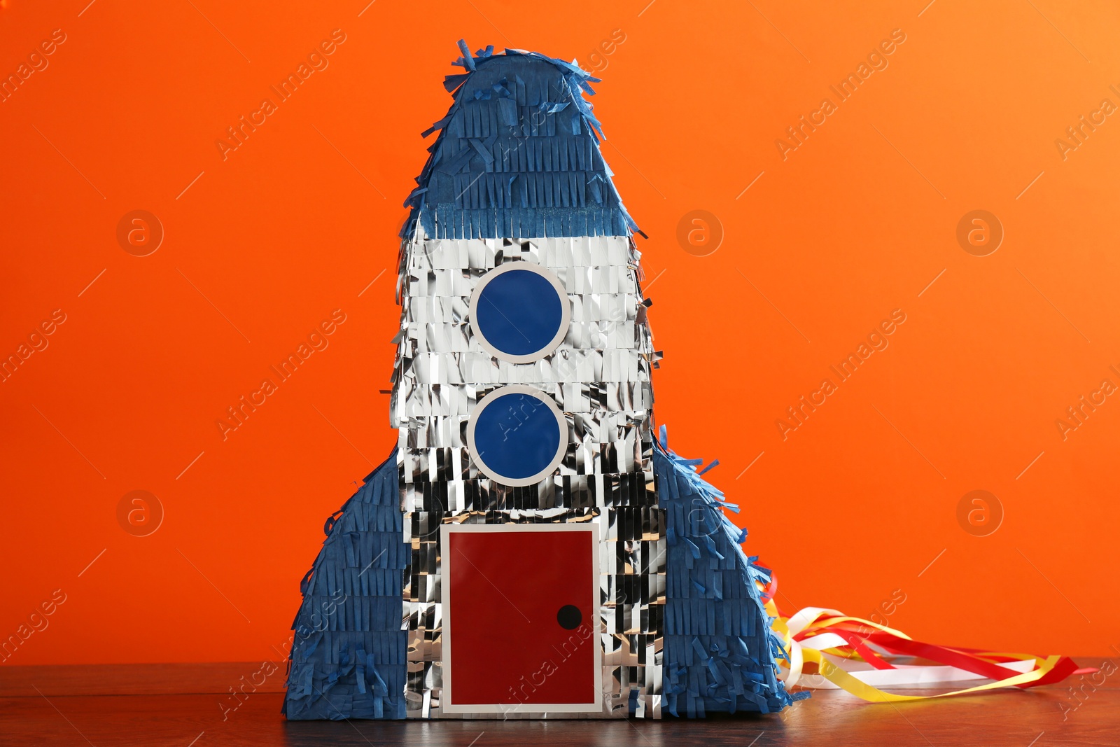 Photo of Bright pinata in shape of spaceship on table against orange background