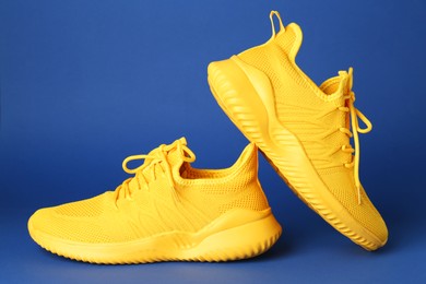 Photo of Pair of stylish yellow sneakers on blue background