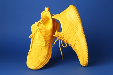 Photo of Pair of stylish yellow sneakers in air against blue background