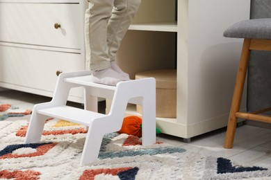 Photo of Little boy standing on step stool at home, closeup