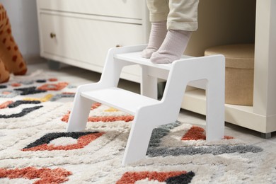 Photo of Little boy standing on step stool at home, closeup