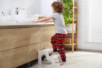 Photo of Little boy with step stool near bathroom vanity indoors