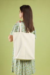 Woman with blank shopper bag on color background, back view. Mockup for design