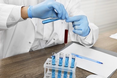 Photo of Scientist with test tubes working at table in laboratory, closeup