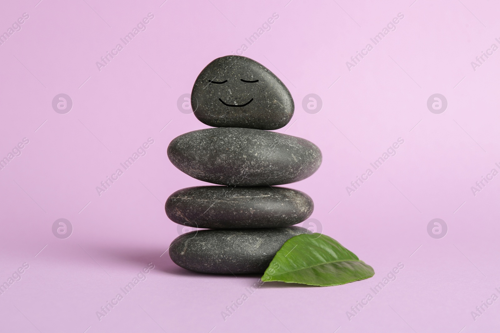 Photo of Stack of rocks with drawn smiley face on lilac background. Harmony and life balance