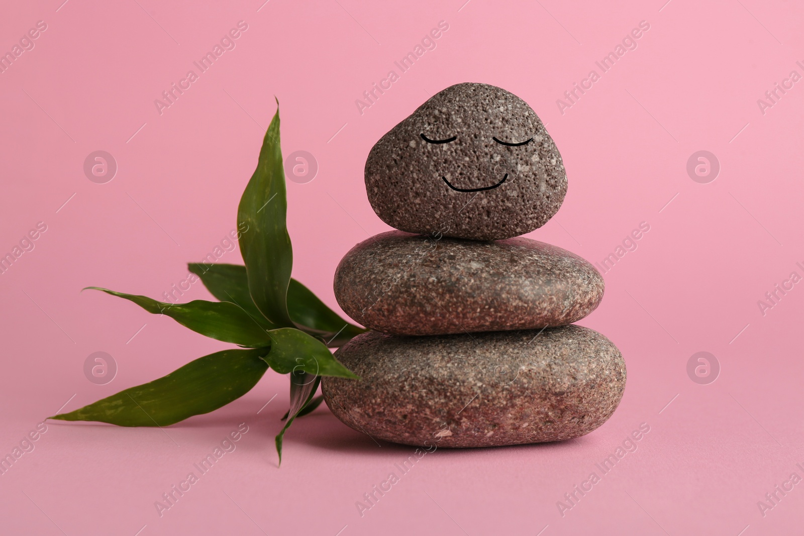 Photo of Stack of rocks with drawn smiley face on light pink background. Harmony and life balance