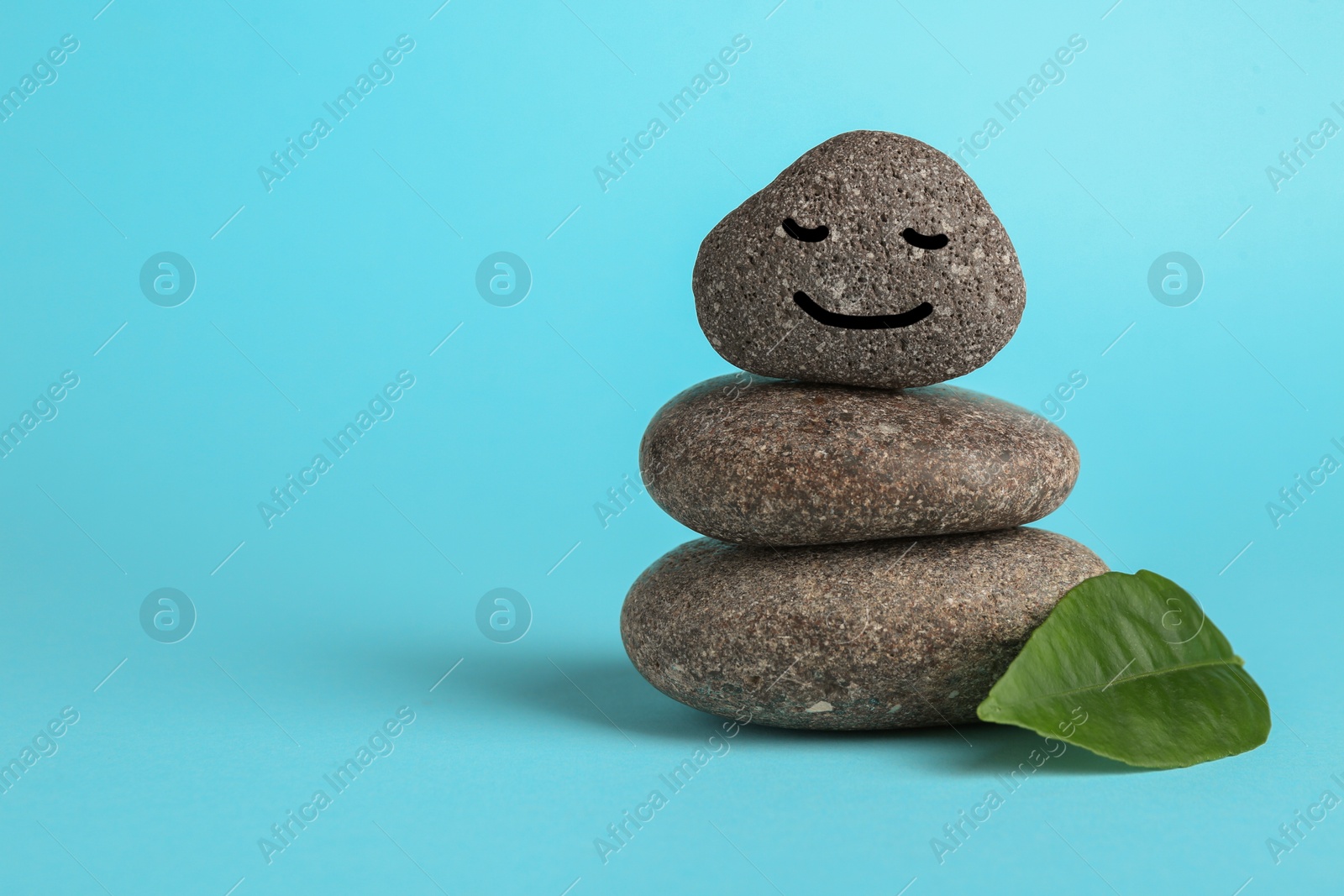 Photo of Stack of rocks with drawn smiley face on light blue background, space for text. Harmony and life balance