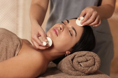 Photo of Young woman receiving facial massage with spa stones in salon