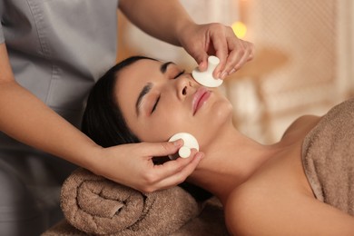 Photo of Young woman receiving facial massage with spa stones in salon