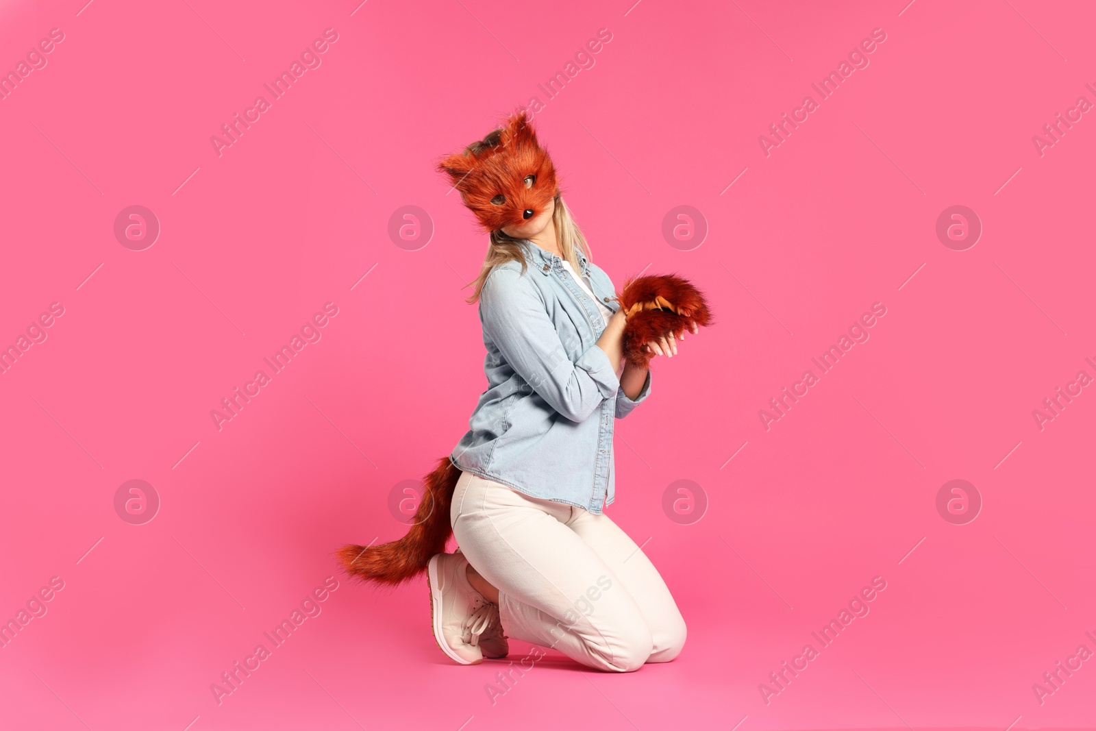 Photo of Quadrobics. Woman wearing fox mask, gloves and tail on pink background