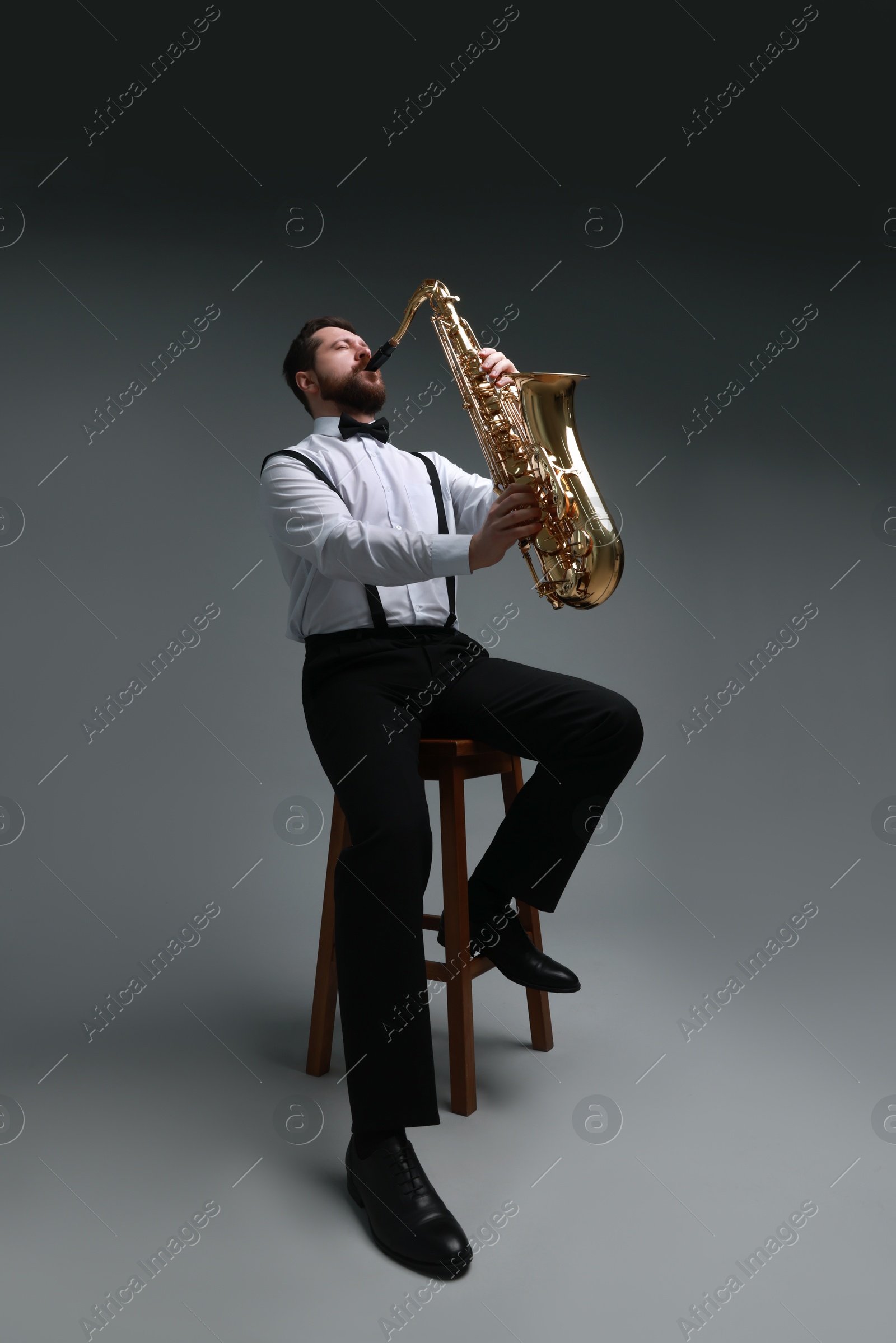 Photo of Professional musician playing saxophone on grey background, low angle view