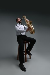 Professional musician playing saxophone on grey background, low angle view