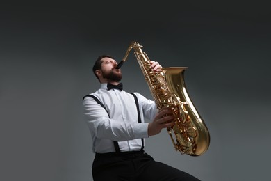 Professional musician playing saxophone on grey background, low angle view