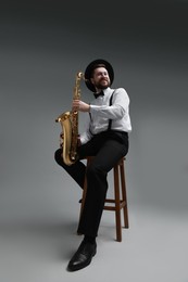 Professional musician with saxophone on grey background, low angle view