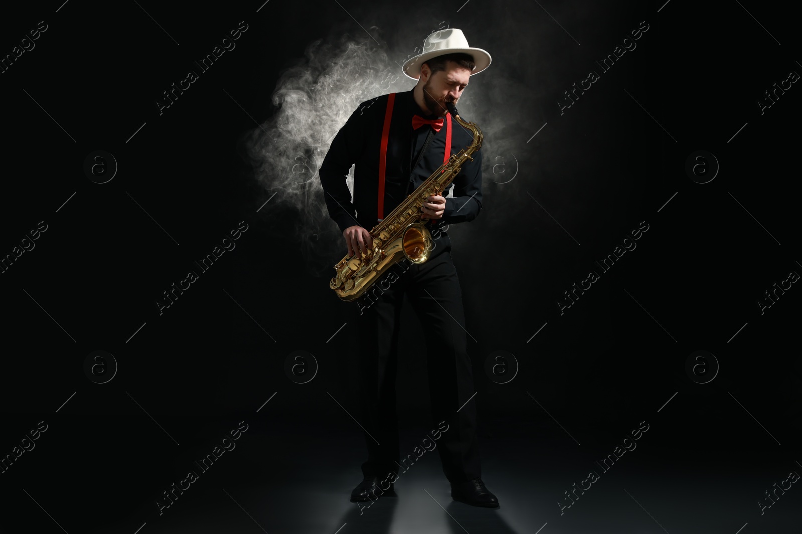 Photo of Professional musician playing saxophone on black background with smoke