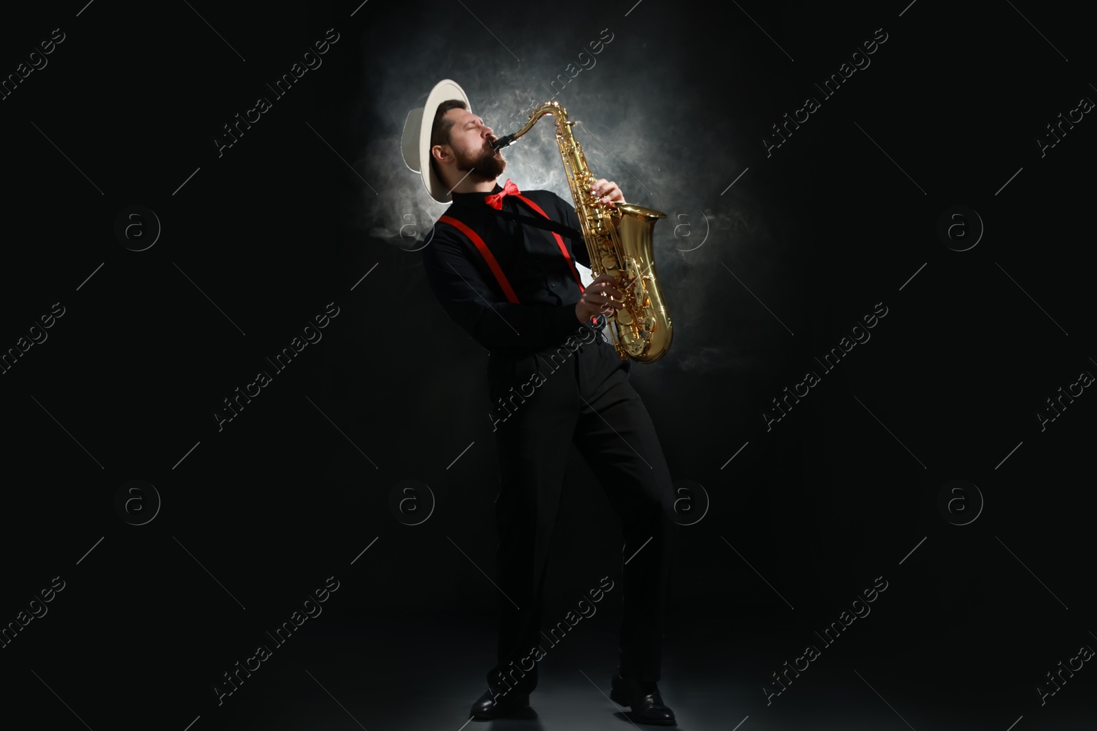 Photo of Professional musician playing saxophone on black background with smoke