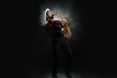 Photo of Professional musician playing saxophone on black background with smoke