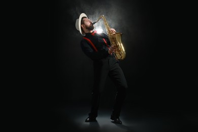 Photo of Professional musician playing saxophone on black background with smoke